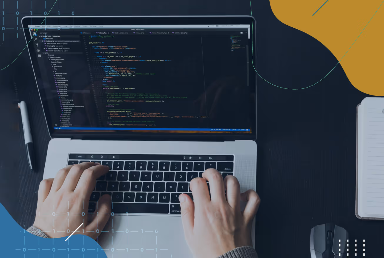 Hands typing on a laptop keyboard displaying code in a text editor on a dark desk with a pen, mouse, and notebook nearby.